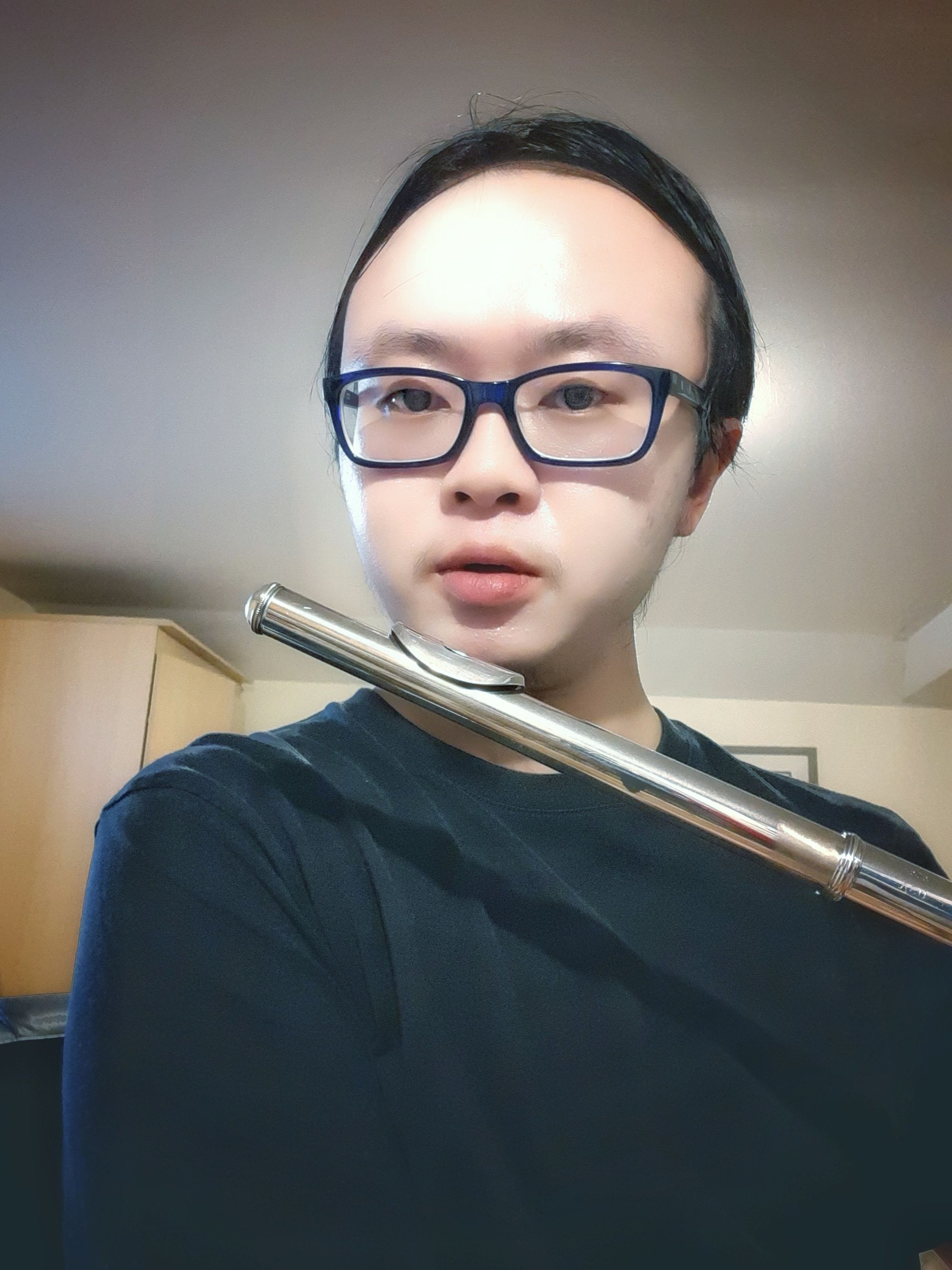 Author with short black hair, purple glasses, wearing a black shirt, holding a flute up as if to play it.