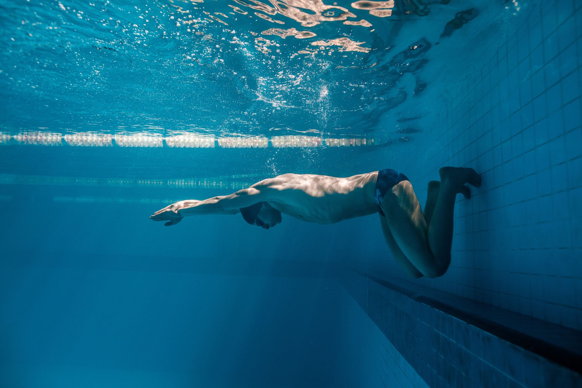 Toned male swimmer underwater, ready to kick off from the deck.