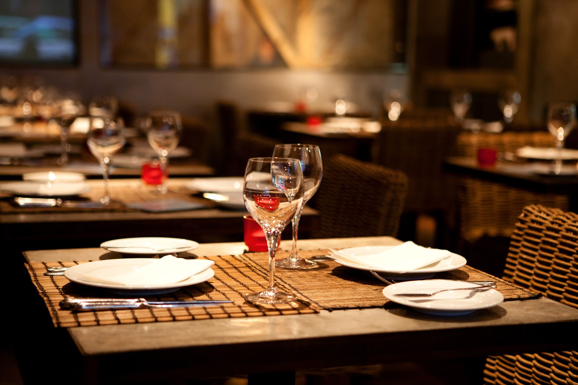 A classy restaurant, with two wine glasses and elegant plates on each table.