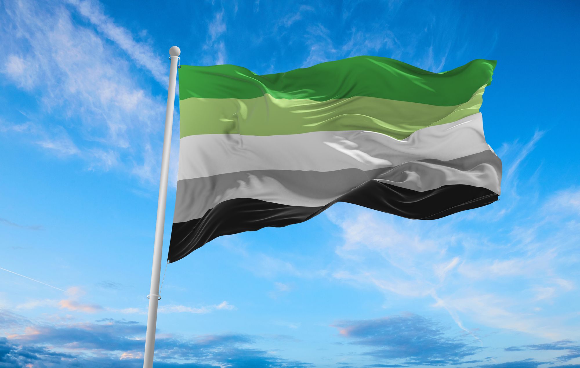 A flag fluttering in the wind against a blue sky. The flag has 5 horizontal stripes. The top stripe is bright green, followed by light green, white, grey, and finally, black at the bottom.