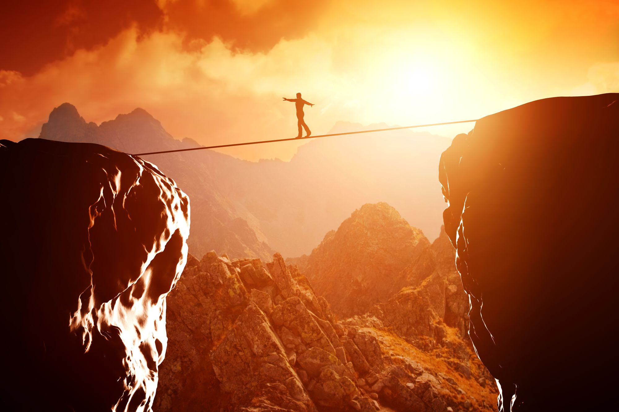 Someone walking on a tightrope across two cliffs.