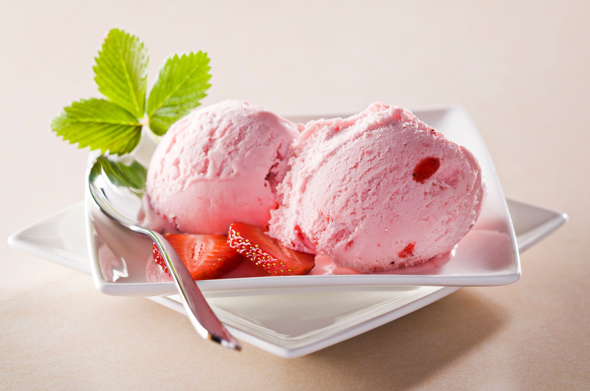 Two scoops of beautiful strawberry ice cream on a fancy white porcelain plate