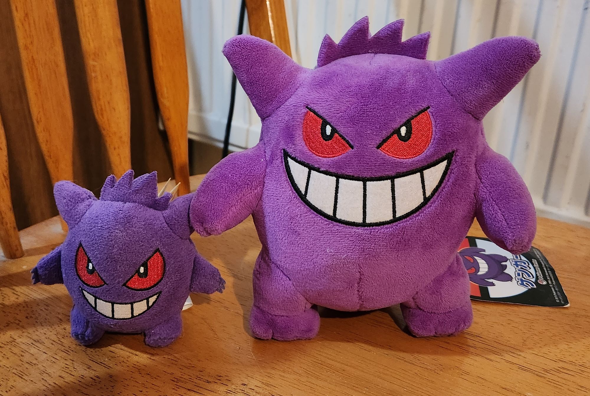 Two purple spiky plushies with red eyes and a wide grin. They are Gengar plushies.