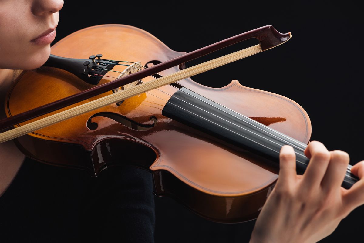 A person is playing a cello with a black background. We can only see the person's hand, chin, nose, and mouth.