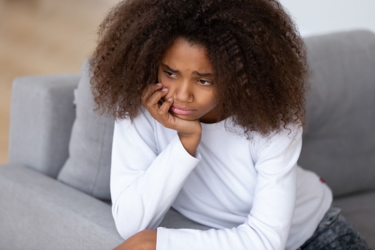 A black girl with frizzy hair rests her chin on her hand, looking glum.