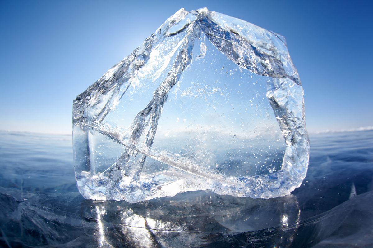 A huge block of ice floating on water, with a bright blue sky in the background.