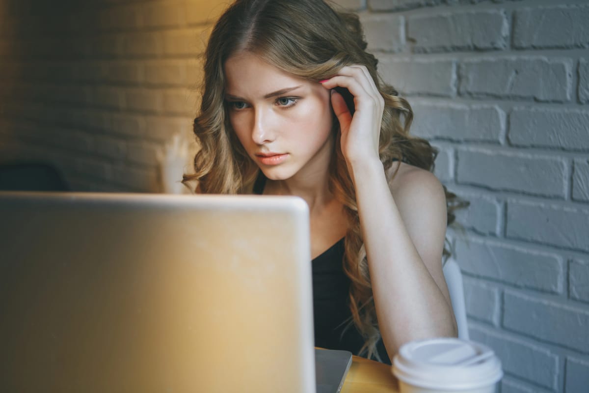 A beautiful girl with long blond curly hair, staring at her laptop.