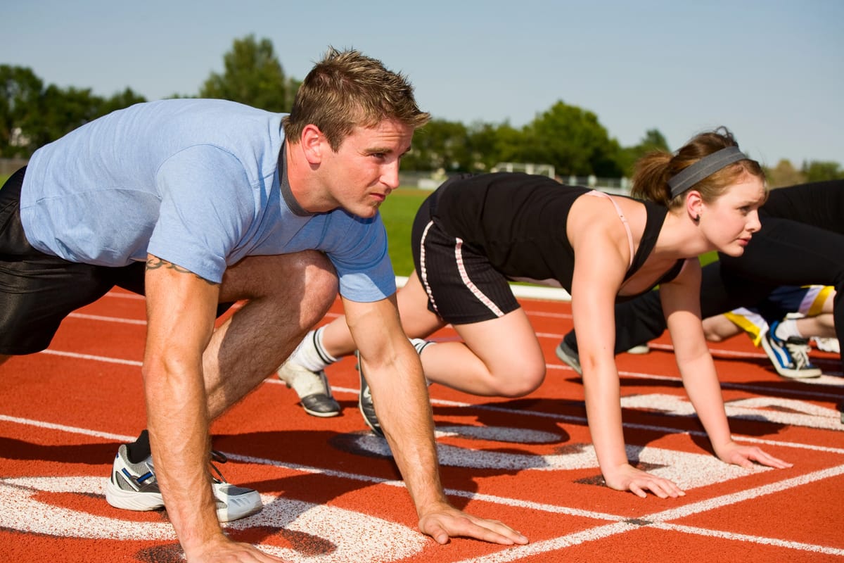 A man, a woman, and some other people out of the camera, are readying themselves for a running race.